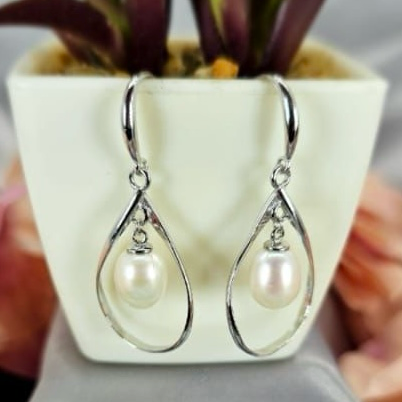 A pair of sterling silver drop earrings with freshwater pearls, displayed on a table next to a potted plant.