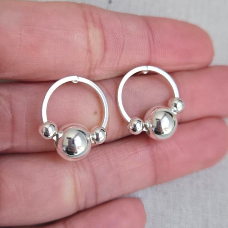 Silver hoop earrings with spherical accents held between fingers on a light background