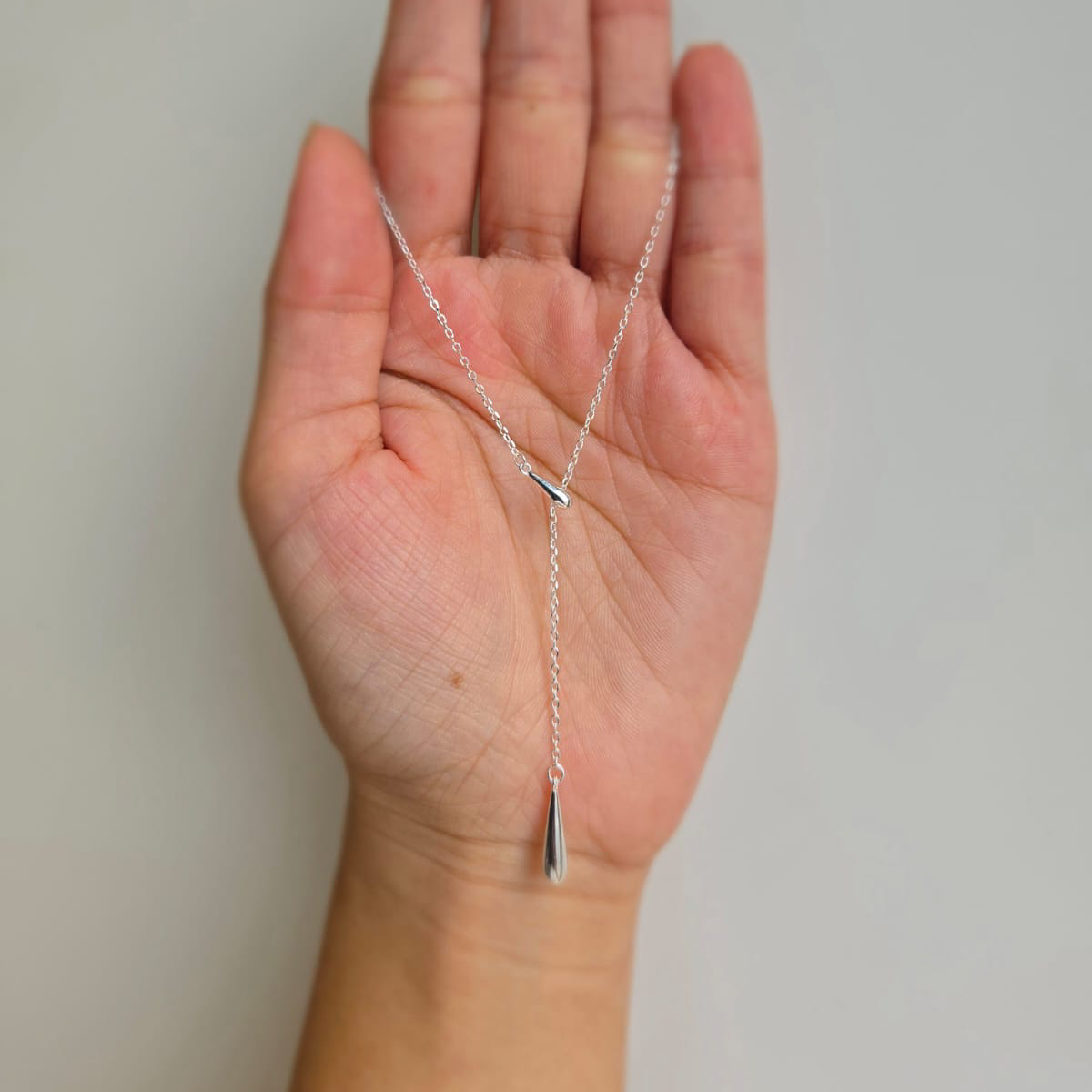 A hand holding a sterling silver necklace with a slider and teardrop pendant.