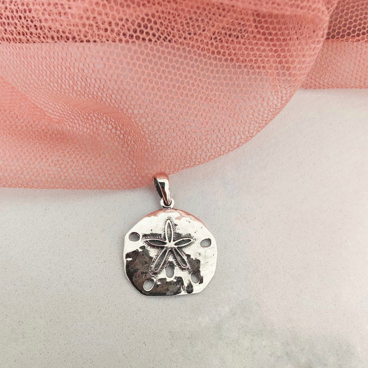 Silver pendant with starfish design on a pink fabric background