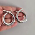 Silver hoop earrings held in a hand against a neutral background