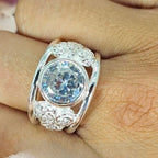 A silver filigree ring with a large cubic zirconia centerpiece displayed on a person's hand.