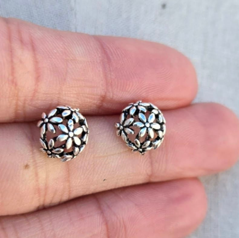 Silver floral patterned earrings held between fingers against a neutral background