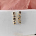 Gold hoop earrings with embedded stones on a white surface with pink fabric in the background