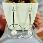 A pair of round circle earrings with moving freshwater pearls, displayed on a surface next to a potted plant.