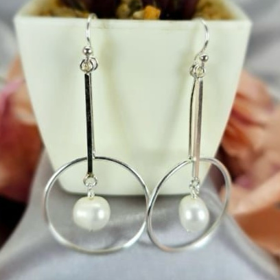 A pair of round circle earrings with moving freshwater pearls, displayed on a surface next to a potted plant.