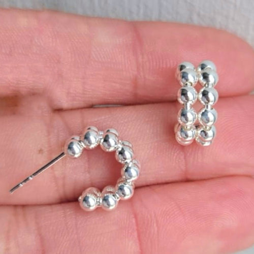 Silver beaded hoop earrings held in a hand against a neutral background
