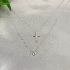 A sterling silver necklace with two layers, one featuring a cross pendant and the other with a crystal pendant, displayed against a light background.