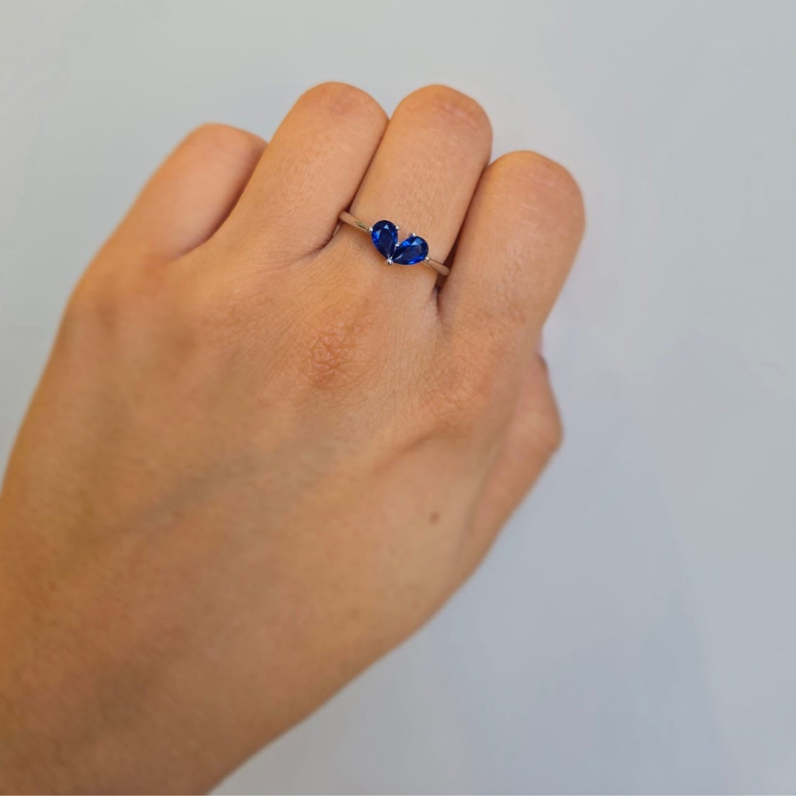 A hand wearing a sterling silver ring with a blue heart-shaped cubic zirconia stone.