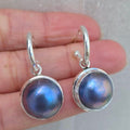 Silver earrings with purple gemstones held between fingers on a neutral background