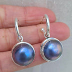 Silver earrings with purple gemstones held between fingers on a neutral background