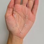 A sterling silver necklace with multiple tiny open heart shapes on a hand, against a white background.