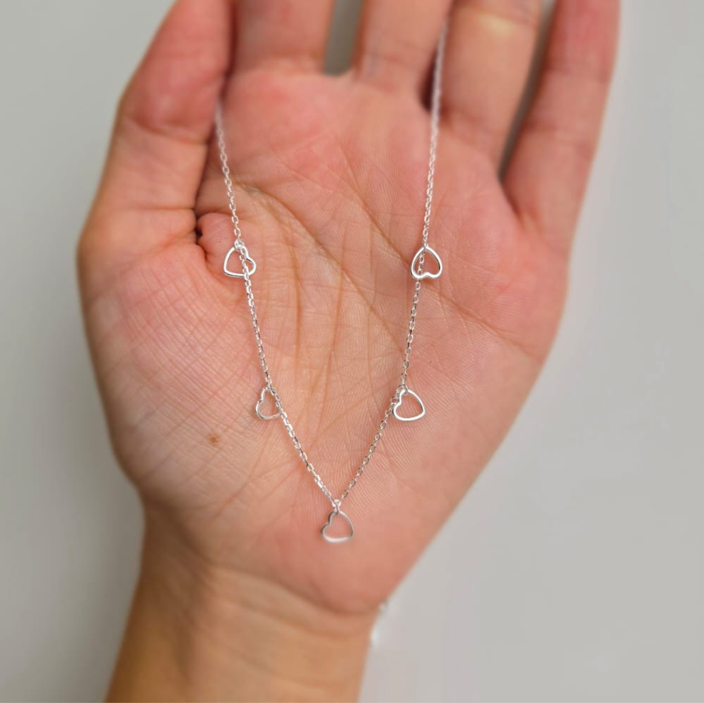 A sterling silver necklace with multiple tiny open heart shapes on a hand, against a white background.