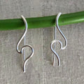 Silver hook earrings on a green stick against a textured fabric background