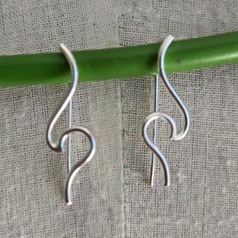 Silver hook earrings on a green stick against a textured fabric background