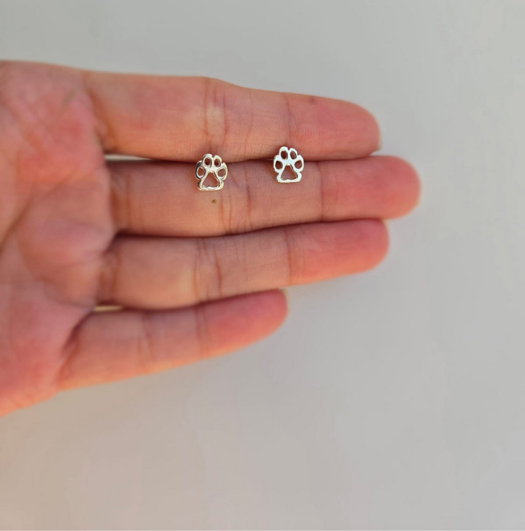 A pair of sterling silver open paw stud earrings held in a person's hand.