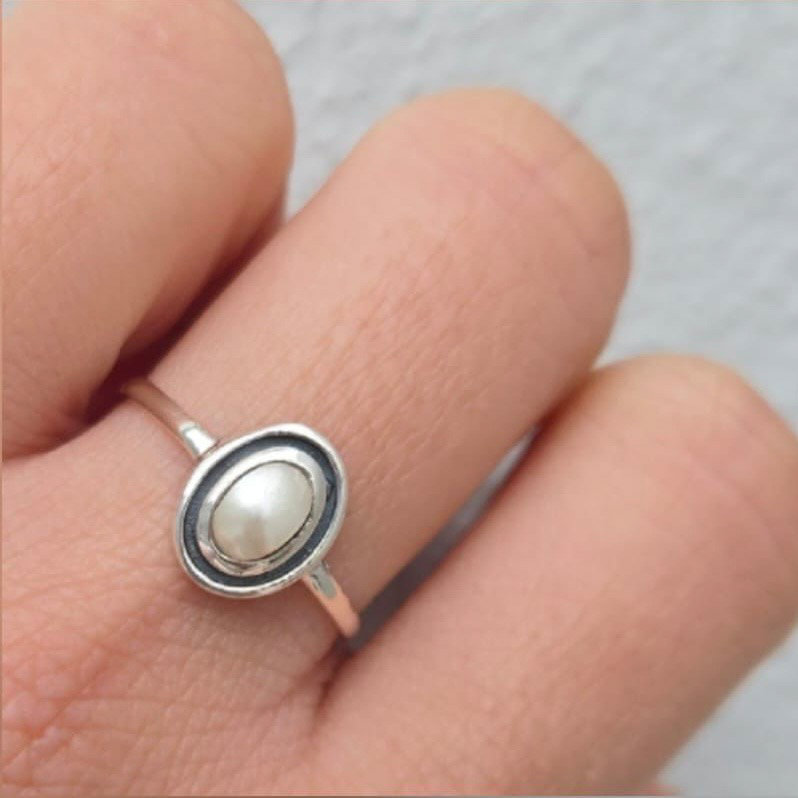 Silver ring with a pearl on a finger against a neutral background