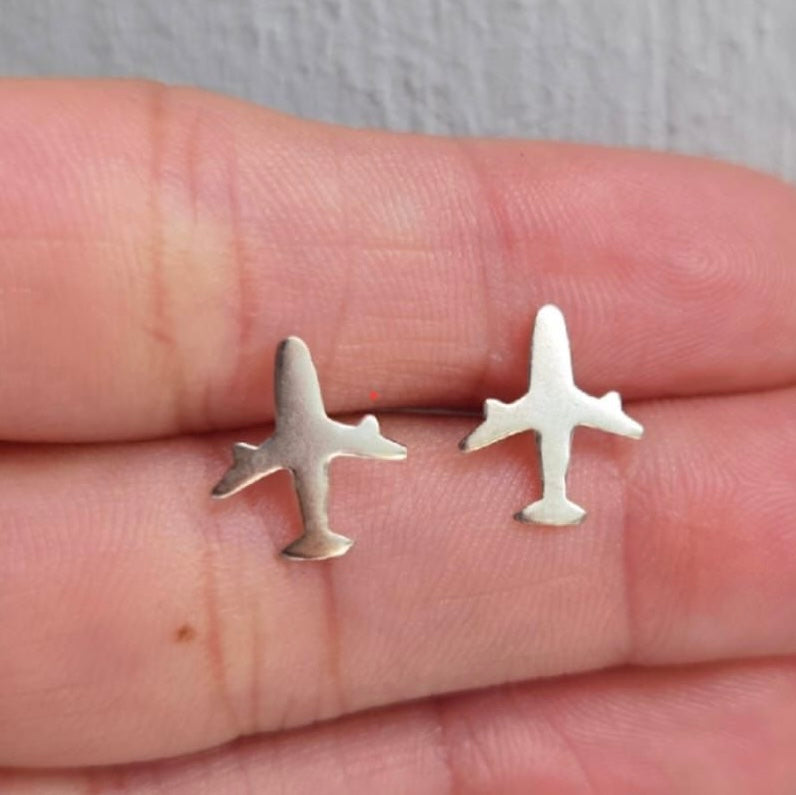 Silver airplane-shaped earrings held between fingers against a neutral background