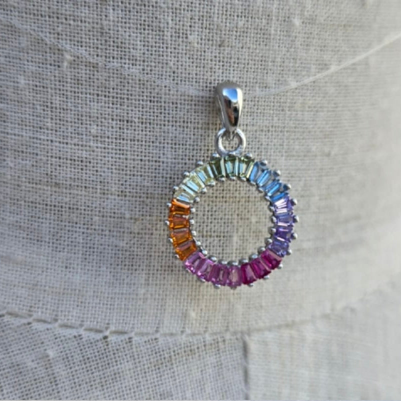 Multicolored circular pendant on a silver chain against a textured gray background
