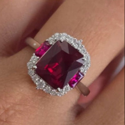 Ring with a large red gemstone and smaller diamonds on a finger