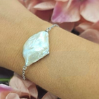 A sterling silver bracelet featuring a large freshwater pearl, displayed on a person's wrist.