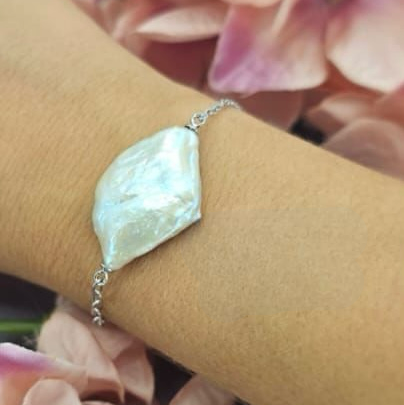 A sterling silver bracelet featuring a large freshwater pearl, displayed on a person's wrist.