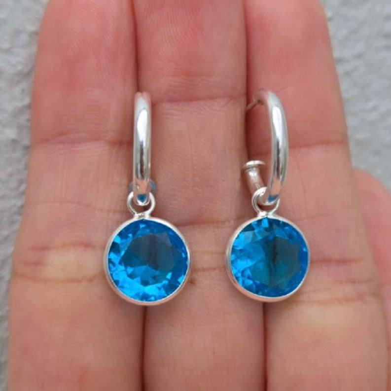 Silver earrings with blue gemstones held in a hand against a neutral background