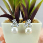 A pair of freshwater pearl earrings with cubic zirconia embellishments, displayed in a white vase with a green plant in the background.