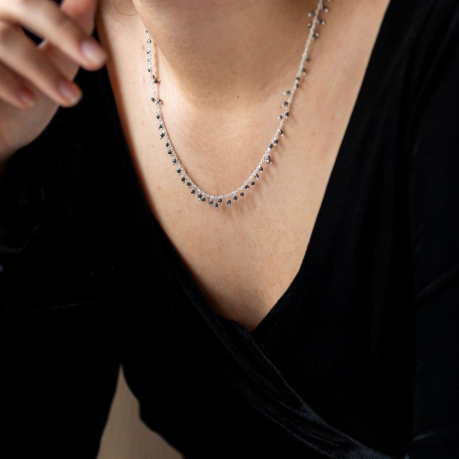 A person wearing a sterling silver necklace with dangling black spinal semi precious stones.