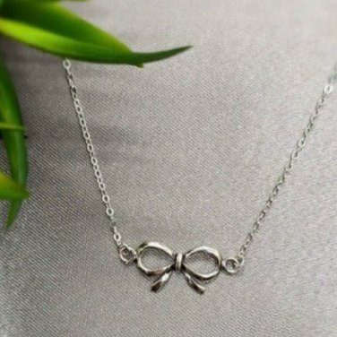 A sterling silver bow necklace displayed on a mannequin, with a smooth finish and a classic bow design.