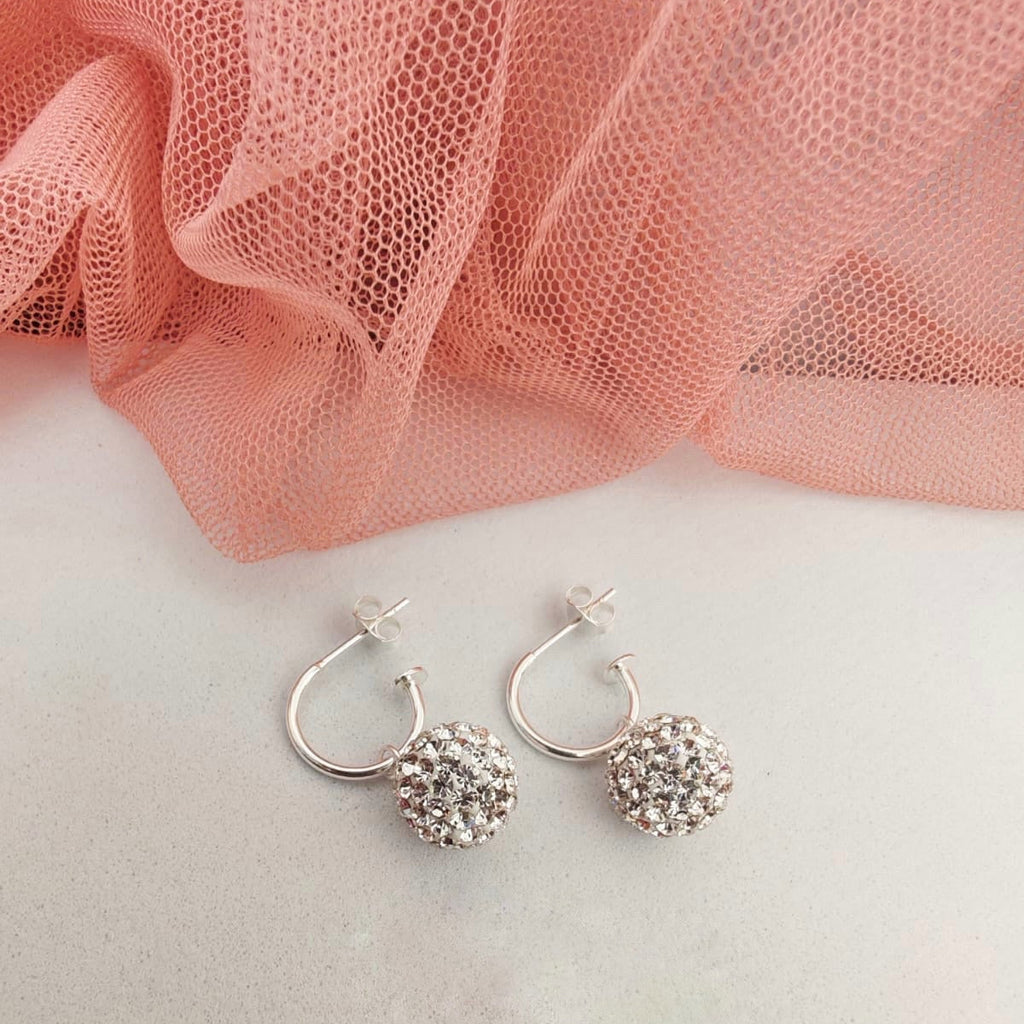 Silver hoop earrings with a textured ball design on a pink fabric background