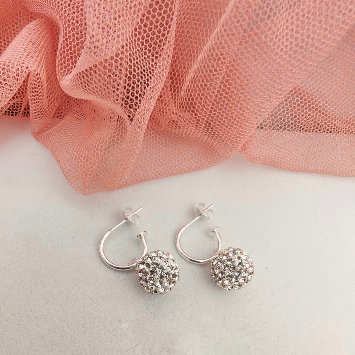Silver hoop earrings with a textured ball design on a pink fabric background