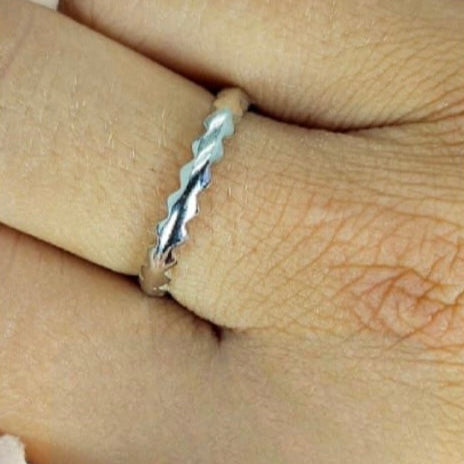 A sterling silver band ring with a textured design, worn on a person's finger.