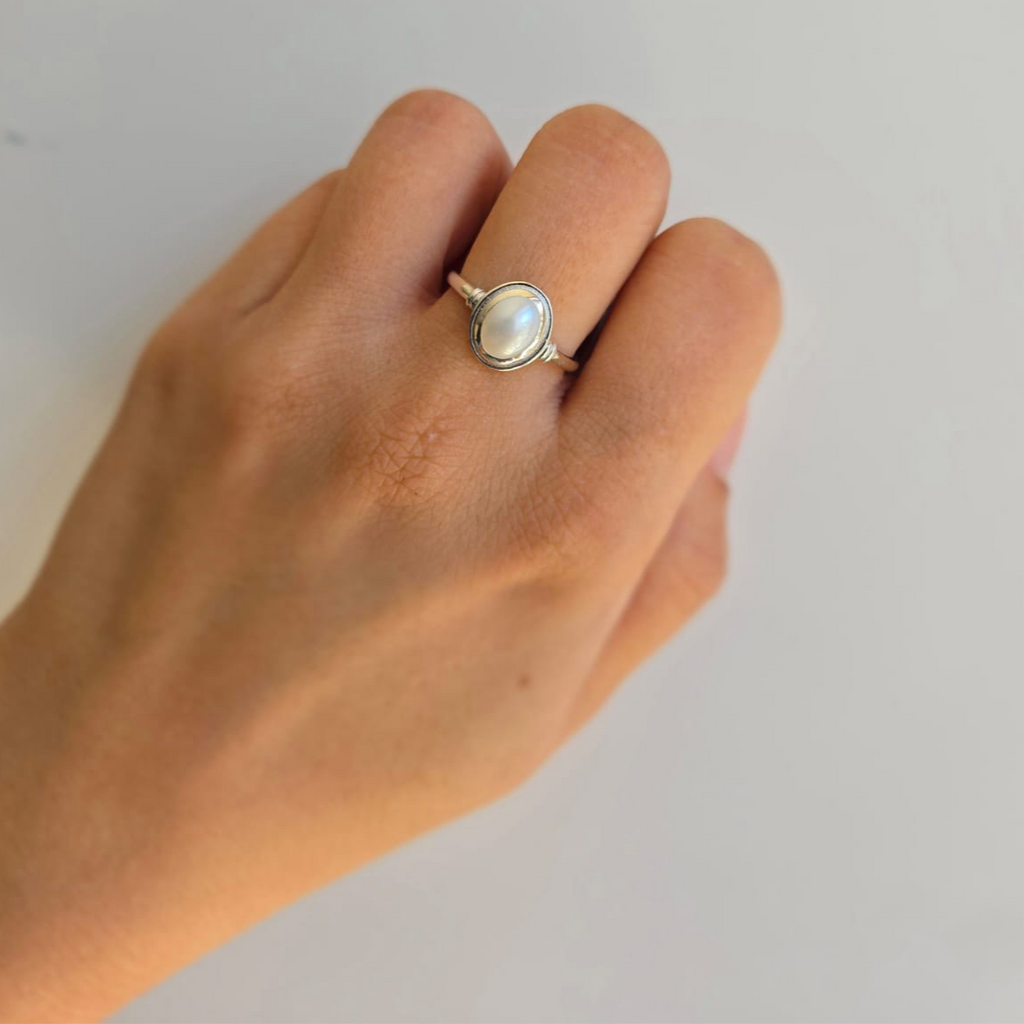 An oval freshwater pearl ring on a person's hand, with a silver band.