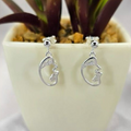 A pair of sterling silver face stud earrings displayed in front of a potted plant.