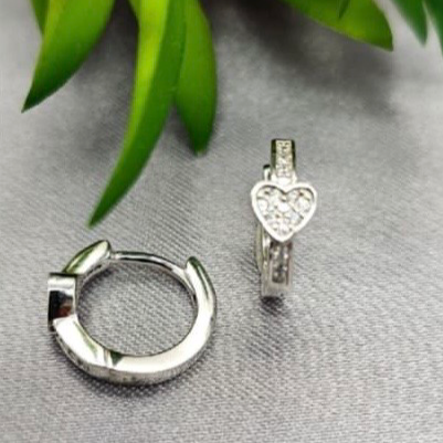 Silver hoop earring and heart-shaped pendant on a gray surface with green leaves in the background