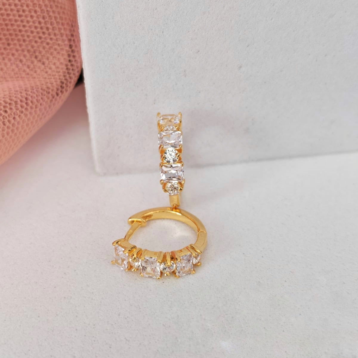 Gold hoop earrings with clear gemstones on a light gray background