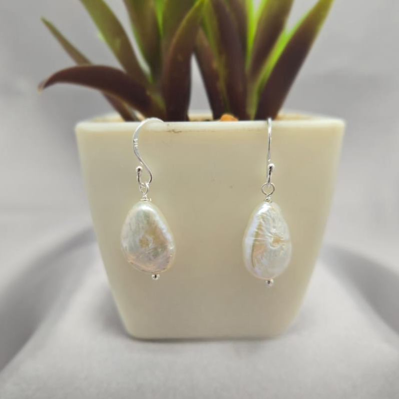 Pearl drop earrings in front of a small potted plant on a light gray background