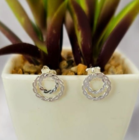 A pair of sterling silver double circle cord stud earrings displayed in front of a potted plant.