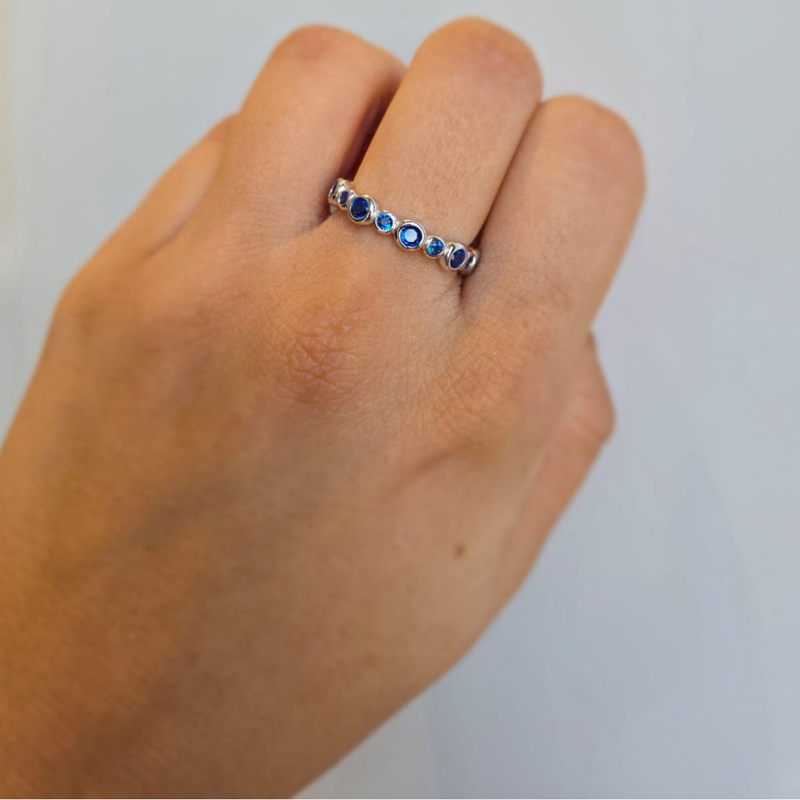 A hand wearing a sterling silver stacking ring adorned with blue cubic zirconia stones.