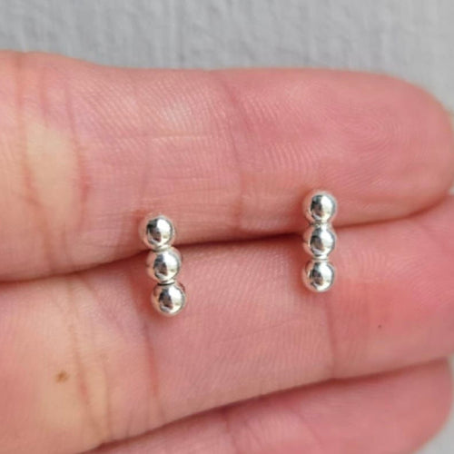 Silver bead earrings on a person's finger against a neutral background