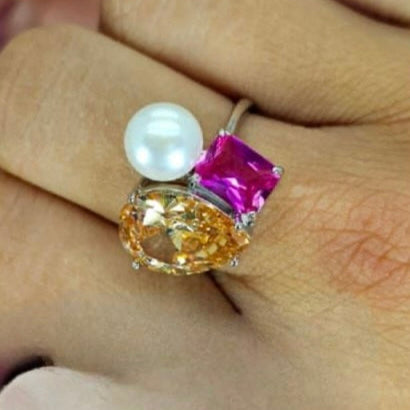 A sterling silver ring with a topaz-colored teardrop, pink rectangular cubic zirconia, and a large freshwater pearl, displayed on a person's finger.