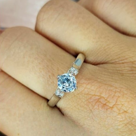 A sterling silver ring with a large cubic zirconia stone in the center, displayed on a person's finger.