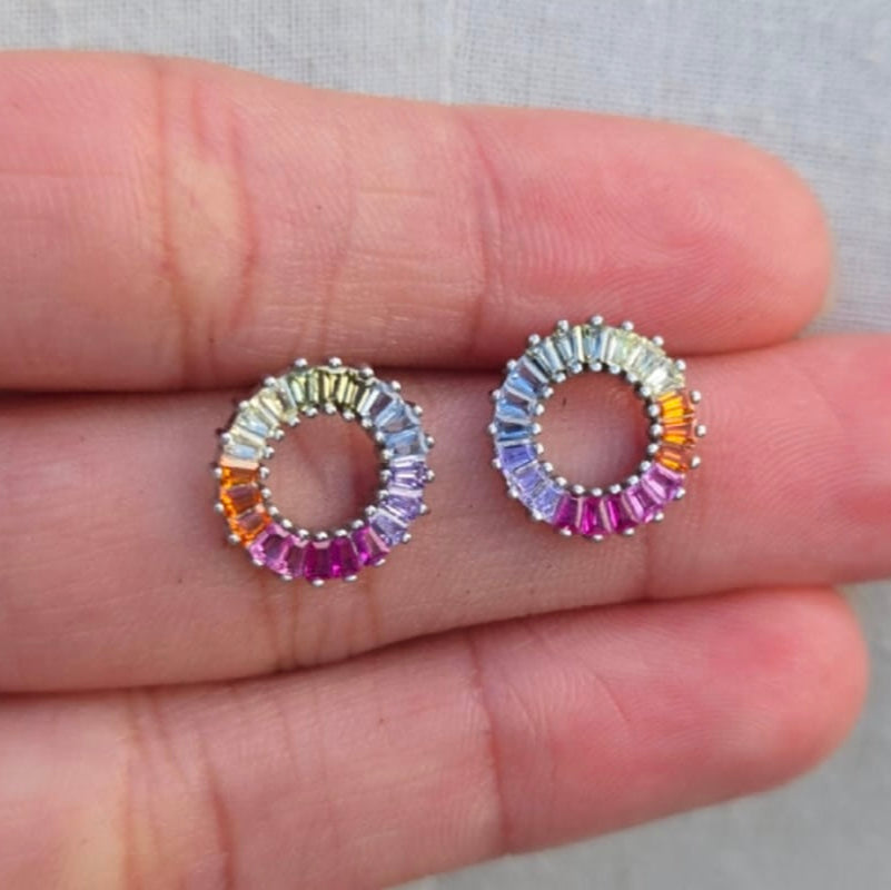 Multicolored circular earrings held between two fingers against a neutral background