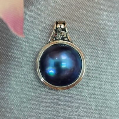 A blue mabe pearl pendant set in a sterling silver mounting, photographed on a grey background.