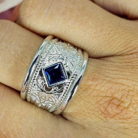 A sterling silver filigree ring with a blue cubic zirconia gemstone in a diamond shape, held on a person's hand.