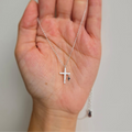A hand holding a sterling silver necklace with two crosses, one large and one small, the large cross being adorned with shimmering crystals.