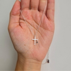 A hand holding a sterling silver necklace with two crosses, one large and one small, the large cross being adorned with shimmering crystals.