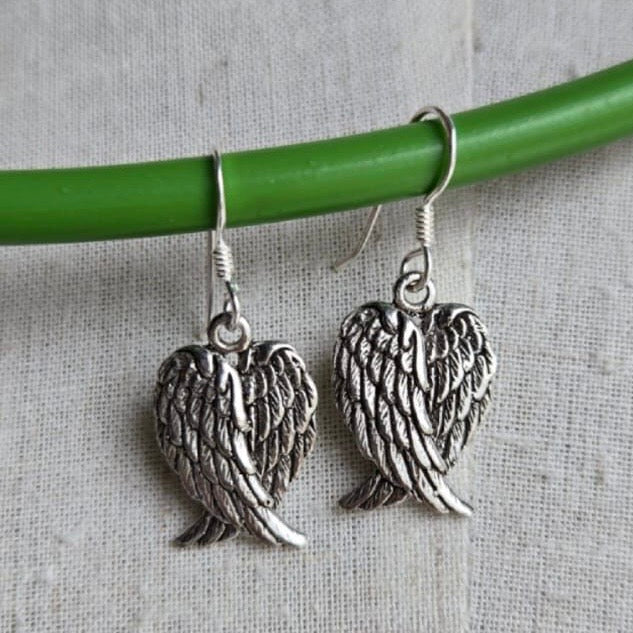 Silver angel wing earrings hanging on a green rod against a textured gray background