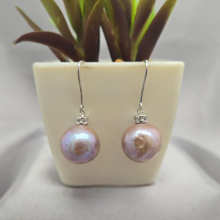 Pearl earrings on a white surface with a small plant in the background